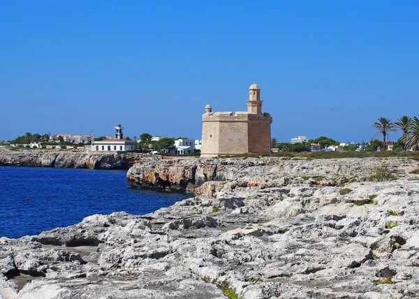ciutadella menorca'da, derin mavi denizi ve kayalık kayalıkları ile kayalıkkayalıkların olduğu kayalıkların ve sahilin parlak güneşli manzarası, uzaktaki tarihi kale ve deniz feneri ile