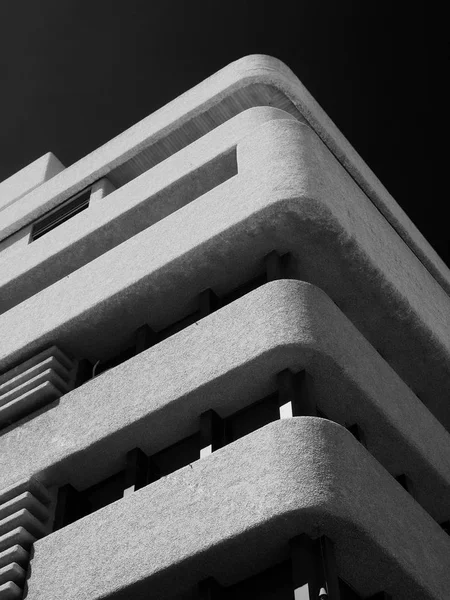 karanlık bir gökyüzüne karşı yuvarlak dokulu köşeleri ile eski bir brutalist beton kule blok monokrom görüntü