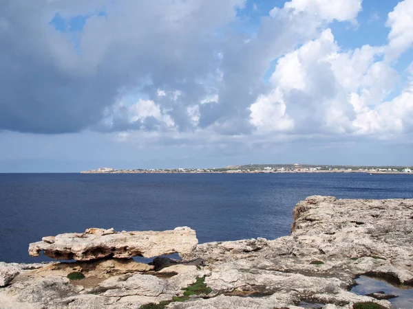 Sahil ve kayalık kayalıkların manzara görünümü sakin bir mavi deniz ve koy boyunca mesafe tatil binaları yansıyan ışık ile ciutalla menorca ayı