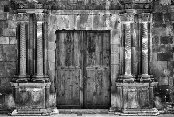 giriş çatlakları ve duvar onarım çevreleyen yıkılmış süslü yivli sütunlar ile eski bir taş binada antik ahşap çift kapı