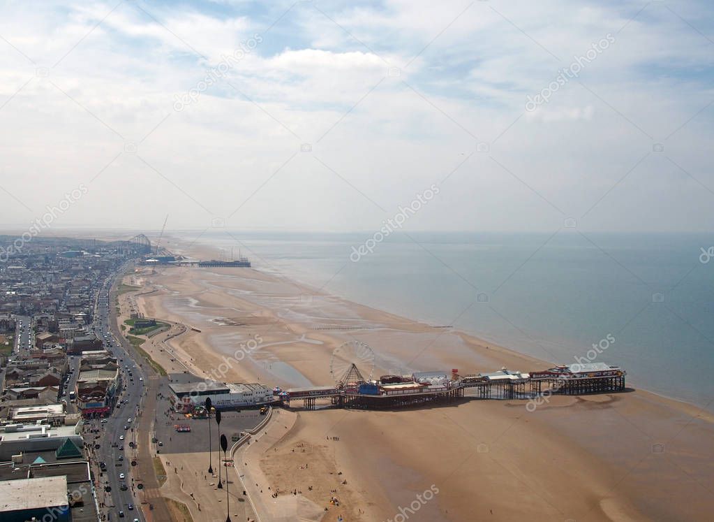an aerial view of blackpool beach looking north showing the south and central piers at low tide with the main road and town stretching to the horizon on a bright summer day with blue sky and clouds
