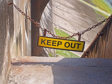 Sarı zincire asılmış levha, yüksek gelgitte sahile çıkan beton deniz duvarının girişini kapatıyor.