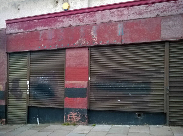 derelict abandoned store with shuttered vandalized shop front with peeling red paint on an urban street
