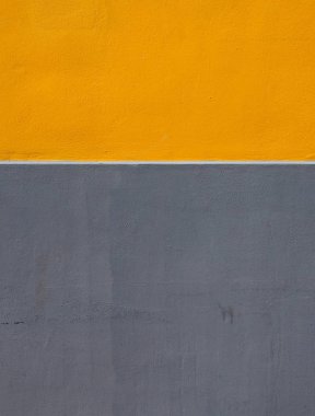 Kaba desenli beton duvardaki sarı ve gri alanlar yatay beyaz bir şeritle bölünmüş.