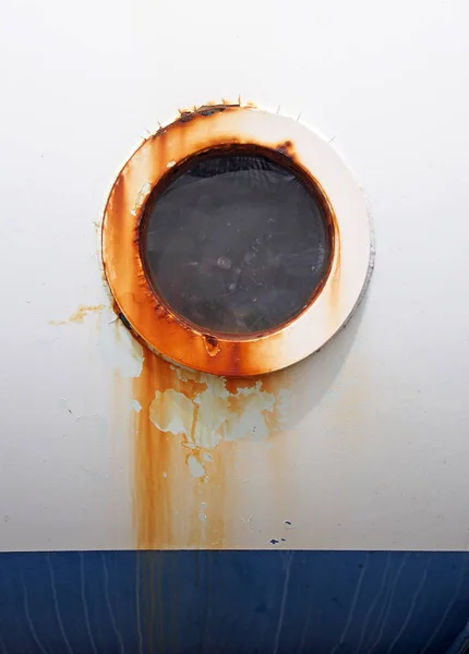 Agujero de buey redondo rayado oxidado en el lado de un viejo barco pintado blanco con superficie azul en la parte inferior —  Fotos de Stock