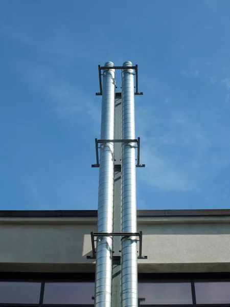 Due camini di estrazione industriale in acciaio lucido sul lato di un edificio contro un cielo blu estivo con luce solare e ombra — Foto Stock