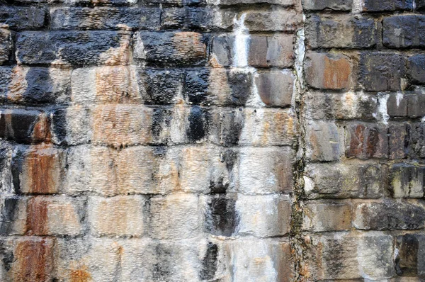 old irregular wet stone wall with damp marks and water streaks of calcified mineral limestone beginning to form in shades of black and brown