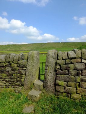parlak mavi yaz gökyüzü ve güneşli çim ile yorkshire dales yamaç çayır adımları ile taş stile veya dar kapı ile kuru bir taş duvar