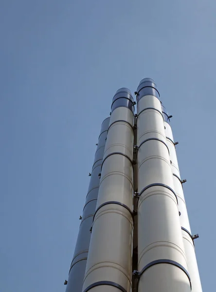 Um grupo de chaminés industriais de aço modernas altas que estão de pé contra um céu azul brilhante e nuvens brancas — Fotografia de Stock