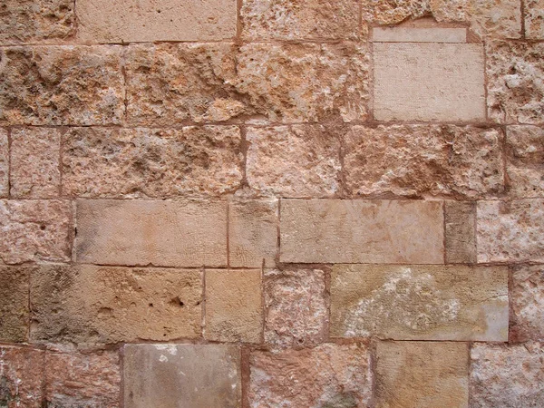 Uma antiga parede de pedra marrom áspera construída de grandes blocos desgastados com pedras danificadas reparadas — Fotografia de Stock