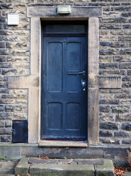 old faded black door with stone door frame and walls with wooden