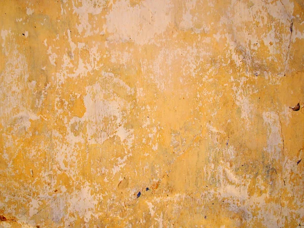 Couches d'écaillage de peinture jaune et beige sur un mur de ciment avec des fissures et des éclaboussures aléatoires d'autres couleurs — Photo