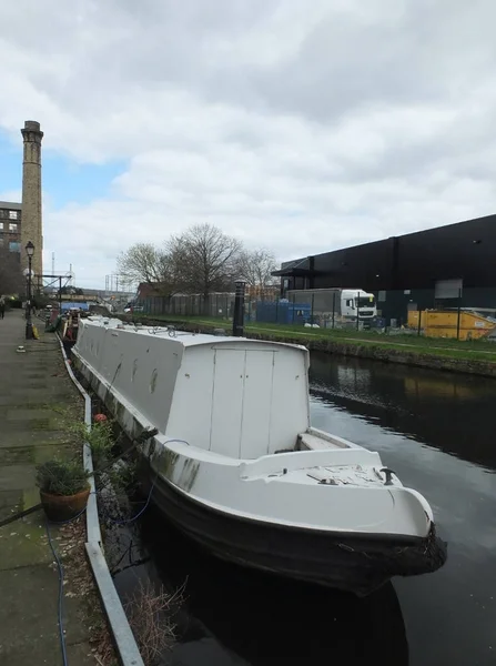 a white narrow boat moored on the canal in an industrial area of huddersfield with moll and bridge in the distance