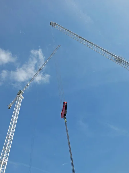 구름이 있는 푸른 하늘을 배경으로 대형 건물 부지에 리프팅 후크와 전선이 있는 두 개의 키가 큰 흰색 건설 크레인의 전경 — 스톡 사진