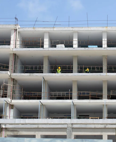 Een grote bouwplaats van residentiële appartementen met witte betonnen wanden en vloeren en arbeiders in beschermende kleding set tegen een blauwe hemel — Stockfoto