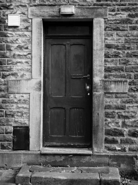 Gammal svart dörr med blekta och bucklig lacken i en stenmur a — Stockfoto