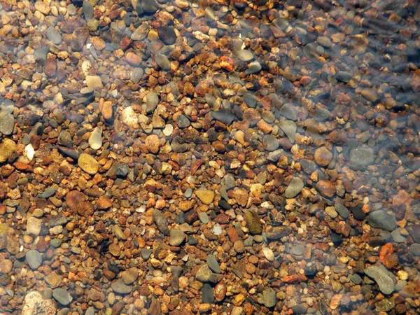 Piedras y guijarros en un lecho de río con agua corriente y ondulaciones — Foto de Stock
