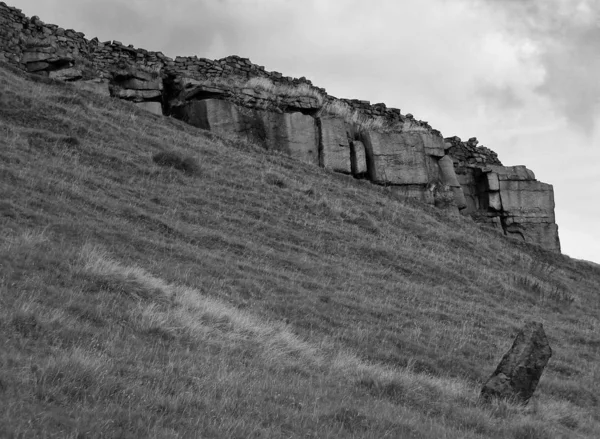 Monochrome image of a large stone outcrop with round stone wall on a hillside with a standing stone in the yorkshire dales — Stock Photo, Image