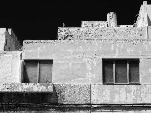 Монохромний старий порожній бетонний будинок в Іспанії з текстурованими тріщинами ліпнини і пілінговою фарбою в яскравому сонячному світлі на тлі чорного неба — стокове фото