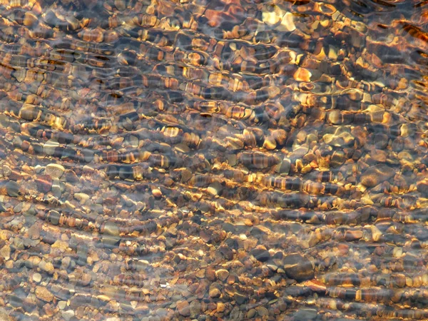 Seixos em água com ondulações em água clara com luz solar marrom a — Fotografia de Stock