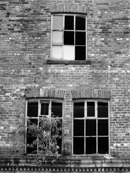 Σπασμένα παράθυρα σε ένα εγκαταλελειμμένο ερειπωμένο κτίριο τούβλων με χόρτο — Φωτογραφία Αρχείου