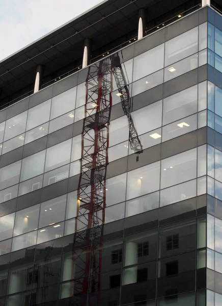 The corner of a modern glass and black office building with reflection of a construction crane on the windows and blue sky — Stock Photo, Image