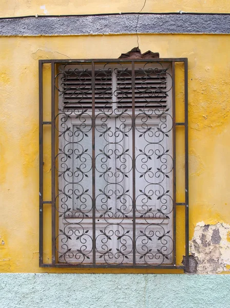 Weiße hölzerne Fensterläden hinter schmiedeeisernen Gittern auf einer Verblendung — Stockfoto