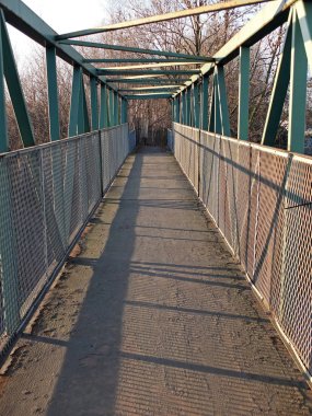 arka planda ağaçlar ile öğleden sonra güneş ışığından gölgeler döküm raylar ve kirişler ile yeşil paslama metal yaya yaya köprüsü boyunca bir perspektif görünümü