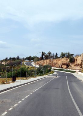 çevreleyen ağaçlar ve mavi güneşte gökyüzü ile mesafe içine bir tepe bükme kaldırımlar ve lampposts ile boş bir iki topal yol