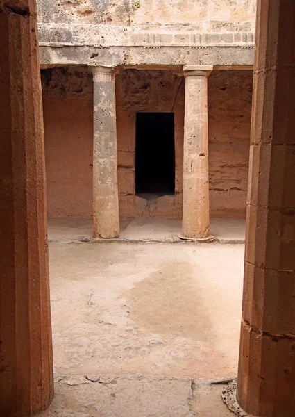 Una cámara subterránea en las tumbas de los reyes en paphos cyprus con viejas columnas de piedra arenisca erosionadas que rodean una puerta vacía oscura — Foto de Stock