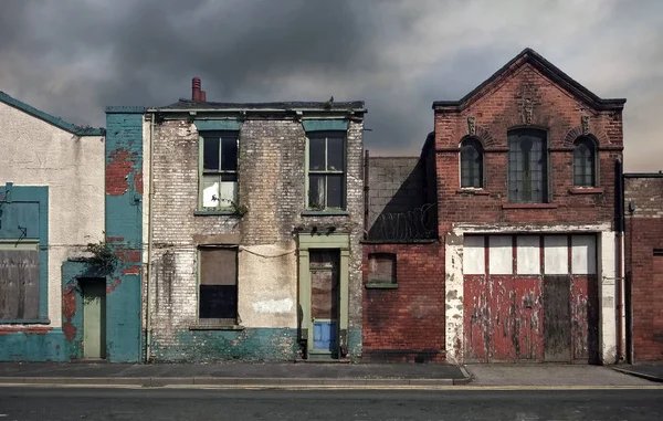 Maisons abandonnées et bâtiments abandonnés dans une rue résidentielle déserte avec des fenêtres barricadées et des murs en ruine contre un ciel gris nuageux — Photo