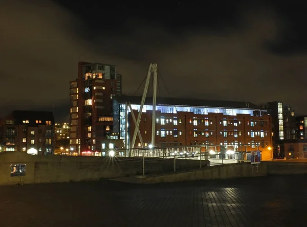 Een stadsgezicht uitzicht op het kanaal toegang tot de Clarence Dock gebied van Leeds met een voetgangersbrug over het water met reflecties van verlichting en gebouwen tegen een nachtelijke hemel met wolken — Stockfoto