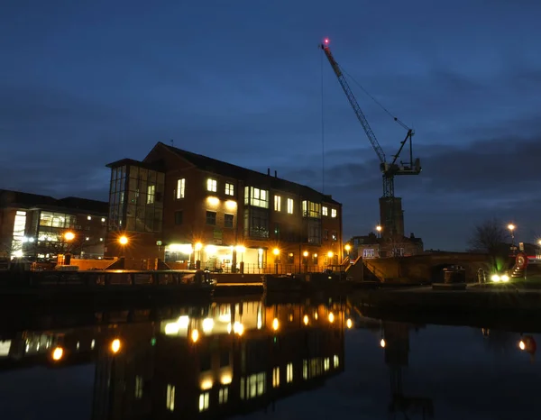 Edificios de oficinas en Holbeck leeds a lo largo del canal por la noche con los edificios reflejados en el agua y el trabajo de desarrollo en el sitio histórico de las obras de la torre visible a través del puente — Foto de Stock