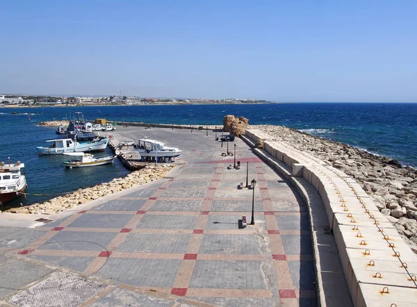Bateaux de pêche et yachts amarrés le long du vieux mur du port de Paphos avec vue sur les bâtiments en bord de mer et la ville au loin — Photo