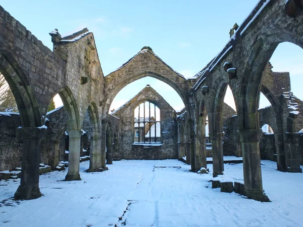 A igreja arruinada medieval em heptonstall coberta da neve que mostra arcos e colunas contra um céu de inverno azul — Fotografia de Stock