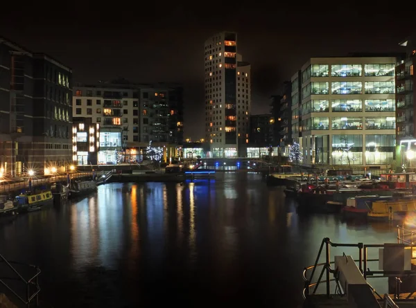 Muelle de clarence en leeds en la noche con edificios brillantemente iluminados reflejados en el agua y barcos amarrados a lo largo de los lados — Foto de Stock