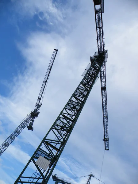 明るい青空と雲に対する大規模な建設現場で作業する高いタワークレーンの垂直ビュー — ストック写真