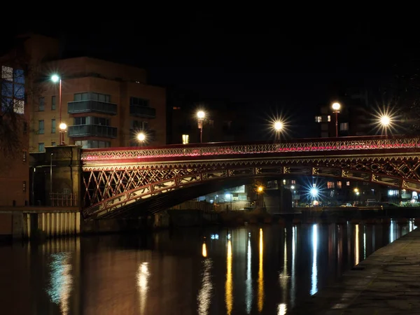 Puente de punta corona cruzando el aire del río en sanguijuelas por la noche con luces y edificios circundantes reflejados en el agua — Foto de Stock