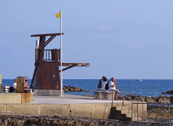 A turisták ültek a sétányon mellett egy életmentő állomás a tengerparton Paphos Ciprus — Stock Fotó