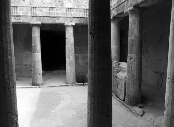 Монохромний кутовий вид підземної кімнати біля гробниць царів у Пафосі з старими еродованими пісковиковими колонами навколо темного порожнього дверного отвору — стокове фото