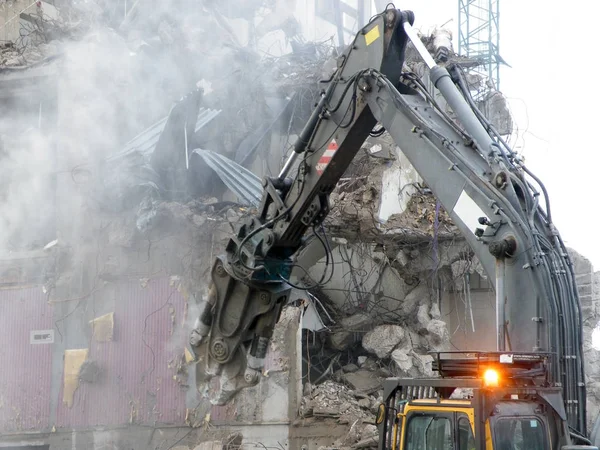 Een mechanische graver met een pneumatische hamer neer te scheuren en oud gebouw op een een stedelijke ontwikkeling site met stof puin en draden zichtbaar — Stockfoto