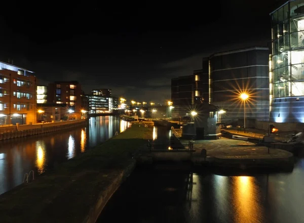 A entrada de fechadura e amarrações no lado do canal de clarence doca em leeds à noite com edifícios da cidade refletida na água e luzes de rua brilhantes — Fotografia de Stock