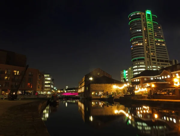 A área do cais do celeiro do canal de leeds à noite com edifícios iluminados refletidos na água com guindastes fechaduras e torres da cidade — Fotografia de Stock