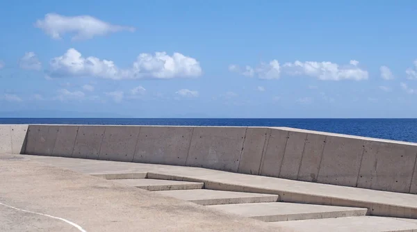 Long image of a concrete sea wall with steps against a calm blue sea and sunlit blue sky — Stock Photo, Image