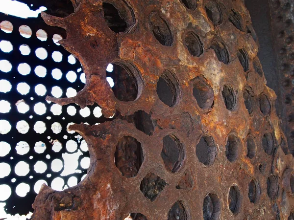 Rusted decaying iron panels covered in round holes with light shining though on obsolete heavy machinery — Stock Photo, Image