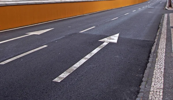 Flechas blancas grandes pintadas en un camino negro de dos carriles con rayas a lo largo de la acera —  Fotos de Stock