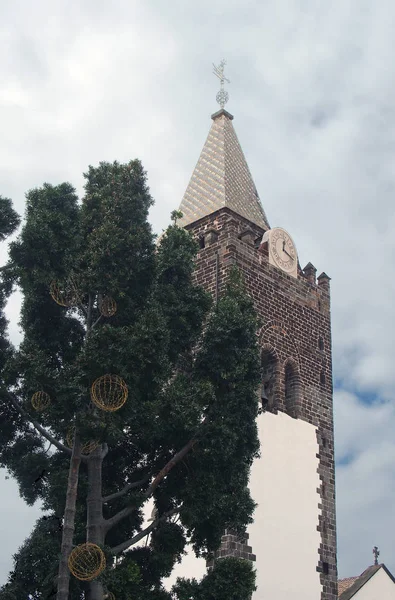 Le clocher de la cathédrale funchale de madère derrière un arbre aux lumières décoratives au ciel nuageux bleu — Photo