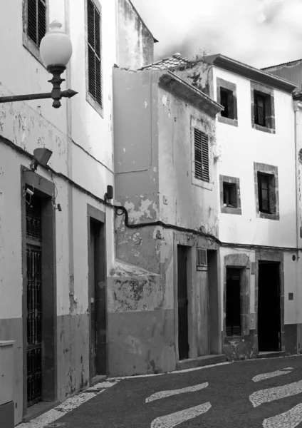 Monochrome image of a typical quiet empty street in funchal madeira with old traditional houses painted in faded peeling paint and a cobbled road — Stock Photo, Image