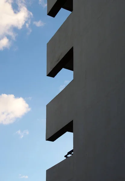 Στη γωνία ενός ψηλού κτιρίου διαμερισμάτων με μπαλκόνια που σχηματίζουν γεωμετρικά σχήματα σε ένα γαλάζιο συννεφιασμένο ουρανό — Φωτογραφία Αρχείου