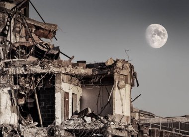 Alacakaranlık akşamı gökyüzünde büyük parlak beyaz bir ay yıkılan beton bir binanın çarpık kalıntılarının üzerinde.
